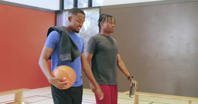 Rising from gym bench, african american men picking up basketball, bottle preparing for practice