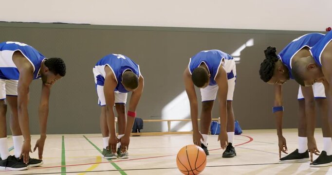 African american male basketball players performing hamstring stretching during warm-up in gym