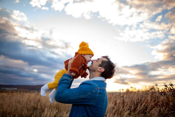 Father's day. Man holding his toddler daughter walking outdoors at sunset. Young parent lifting...