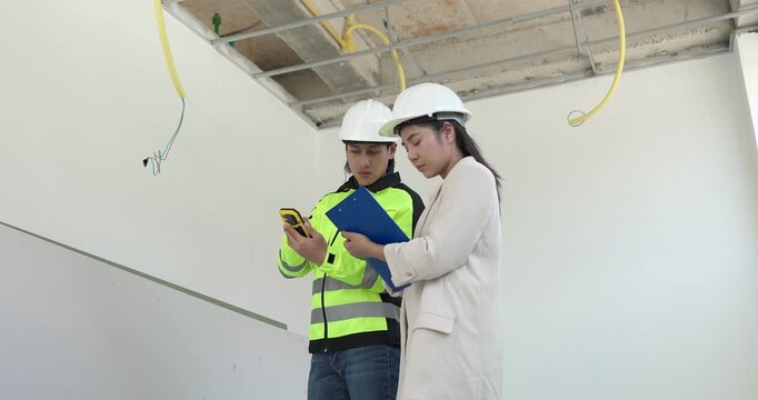 Site engineer and interior designer inspect exposed wiring and ceiling framework at a residential construction site, checking electrical readiness and coordinating renovation work before finishing.
