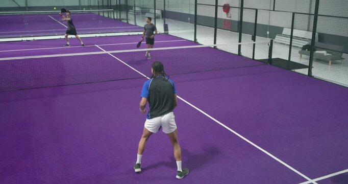 Male players tossing ball serving volley on paddle court rallying foot bump handshake