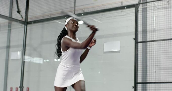 Diverse female teammates volleying incoming padel ball and executing forehand shots on glass court