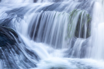 Obraz premium A close up view of a beautiful smooth cascading waterfall flowing gracefully over dark rocks and green aquatic plants.