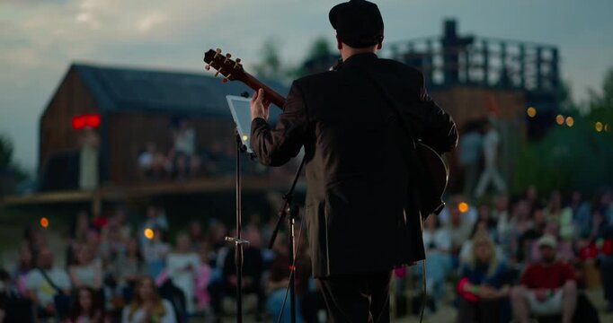 Male acoustic guitarist on outdoor festival stage at sunset