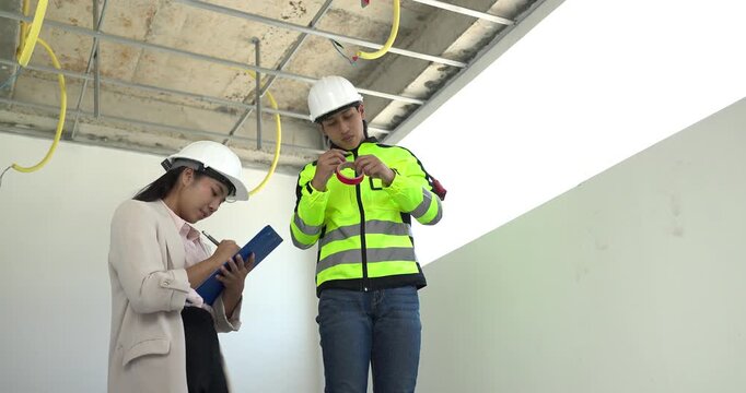 Site engineer and interior designer inspect exposed wiring and ceiling framework at a residential construction site, checking electrical readiness and coordinating renovation work before finishing.
