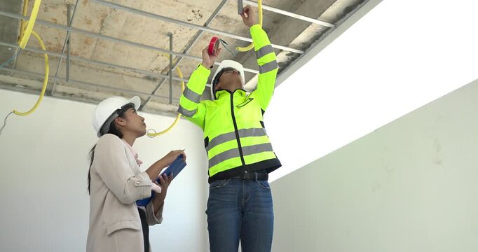 Site engineer and interior designer inspect exposed wiring and ceiling framework at a residential construction site, checking electrical readiness and coordinating renovation work before finishing.
