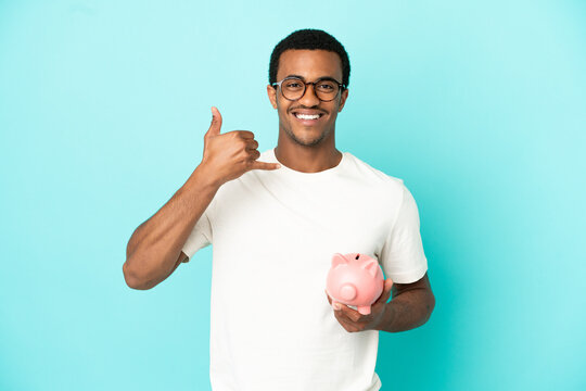 African American handsome man holding a piggybank over isolated blue background making phone gesture. Call me back sign