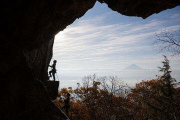 Fototapeta premium Silhouette of rock climbers on a cliff framed by cave opening with Mount Fuji and autumn foliage in Japan