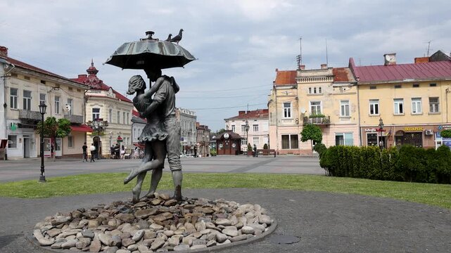 Statue of a young couple kissing under an umbrella known as the lovers fountain on Zamkova Gora square in Drohobych, Western Ukraine, with a pigeon landing on top on a summer day.