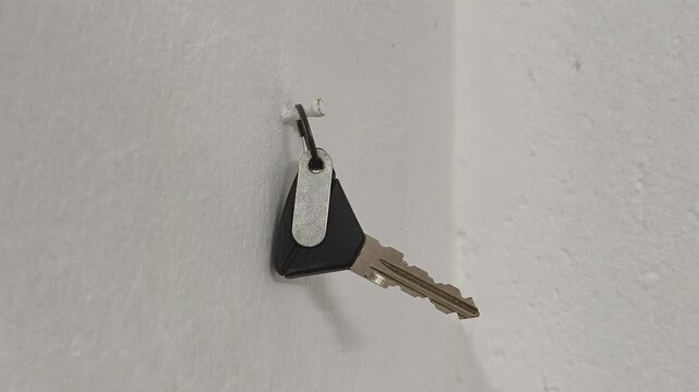 Closeup of rider person hand hang motorbike vehicle key on white cement wall nail. Minimalist or simple lifestyle concept.