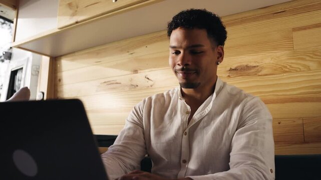 Young man using his laptop inside a camper van. Digital nomad enjoying the freedom of working remotely while traveling on a road trip