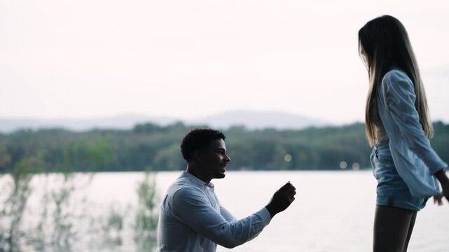 Young man getting down on one knee and asking his girlfriend to marry him with a ring. An emotional moment of proposal, embrace, and happiness