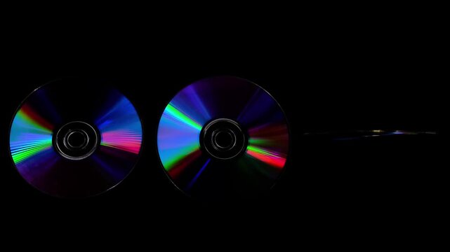 Rainbow light reflecting of a surface of a rotating CD-DVD disk against a dark background, highlight their reflective surfaces in different ways