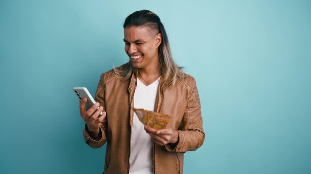 Ecstatic young man with long hair winning money online using his smartphone. He joyfully throws a wad of euro banknotes at the camera