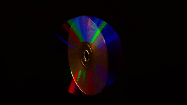 Rainbow light reflecting of a surface of a rotating CD-DVD disk against a dark background, highlight their reflective surfaces in different ways