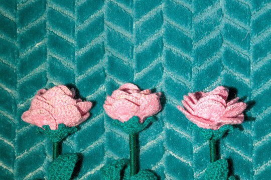Handcrafted pink knitted roses placed on green fabric