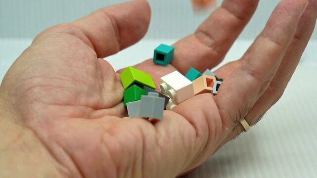 Various small, colorful toy building bricks falling into the open palm of a person's hand, isolated on a white background, representing collecting, hobby, nostalgia, and childhood memories