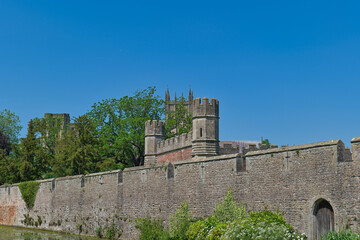 A historic stone castle wall with a prominent turret and distant spires stands against a clear blue sky - The Bishop's Palace & Gardens - Wells - Somerset - UK © Robert