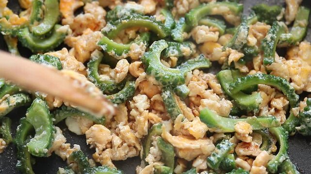 Stir-frying scrambled eggs with sliced bitter melon using a spatula in a hot pan. Healthy Thai food