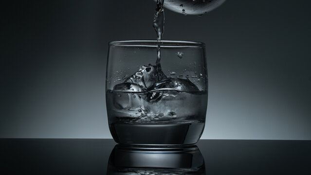 Moody backlit whiskey glass with fresh water splash and ice cubes on dark mirror surface