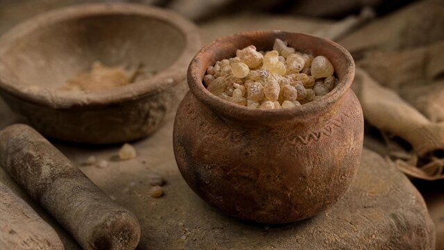 Ancient terracotta pot containing resin pieces with grinding tools, warm lighting.