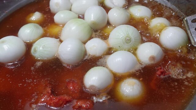 Close-up of meat and white onions cooking in bubbling oil with sausages