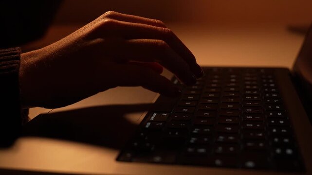 Hands typing on laptop keyboard in warm moody lighting close up
