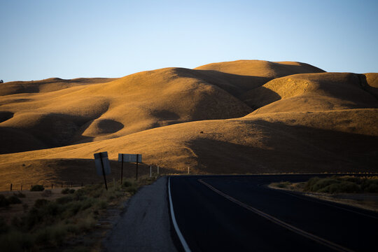 Empty highway through golden rolling hills at sunset