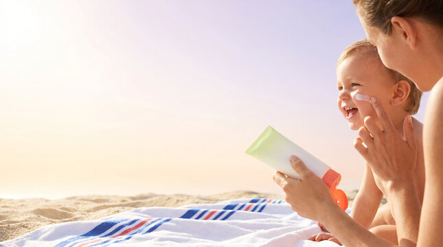 Mother applying sunscreen on baby while smiling on the beach  