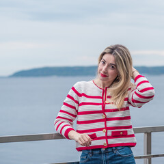 Fototapeta premium Elegant lady in red and white striped cardigan by the water. Spring lifestyle fashionable portrait