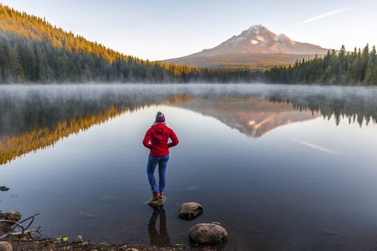 Young woman looking at view of volcano Mt. Hood with reflection in lake Trillium Lake, at sunrise, Oregon, USA