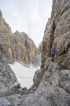 Mountaineer climbs on a steep rock face in the Via Ferrata dell'Ideale via ferrata, spectacular mountain landscape with steep rock faces at the Bocca d'Ambiez, remnants of the Vedretta d'Ambiez glacier, Brenta Mountains, Parco Naturale Brenta-Adamello, Trentino, Italy