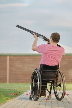 Rear view of a man in a wheelchair aiming at a clay pigeon at outdoor shooting range