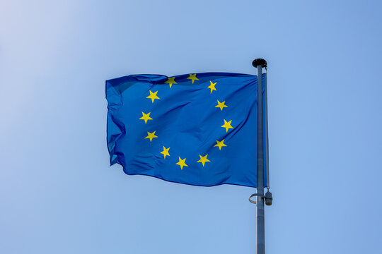 The flag of Europe on the pole waving in the air with blue sky as background, European union flag consists of twelve golden stars forming a circle on a blue field, A symbol for the whole of Europe.