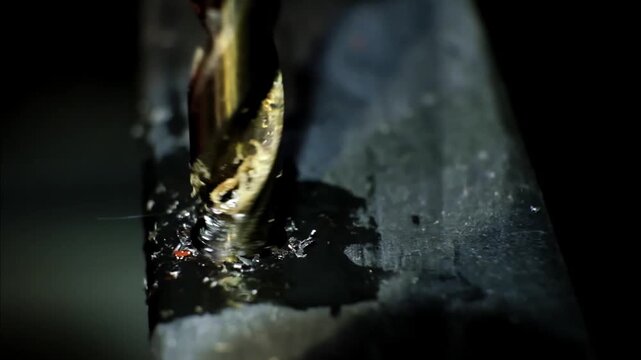 Close-up macro shot of a metallic twisting drill bit drilling a dark metallic surface, stained with metal shavings and lubricant. Metal processing. Construction works. B-roll 4K slow motion footage