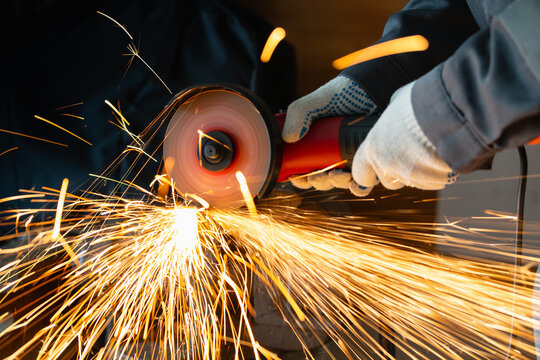 a worker in gloves cutting metal with an angle grinder tool in a workshop