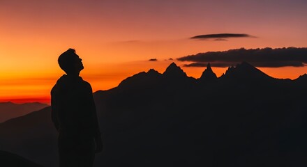 Obraz premium Silhouetted Person Standing Against Dramatic Mountain Sunset Landscape