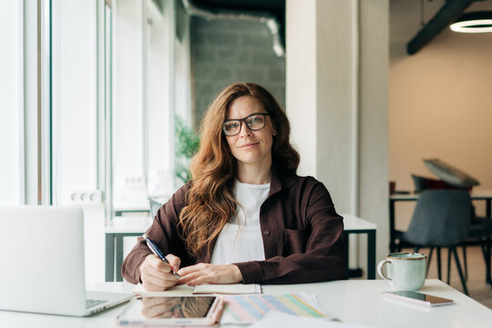 Confident woman working at a modern desk writing notes in a bright coworking workspace