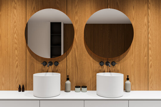 Modern bathroom interior with dual round mirrors, wooden wall panels and minimalist white sinks in contemporary design. 3D Rendering