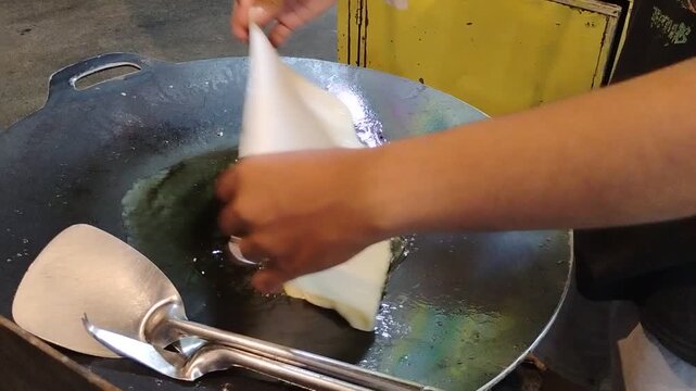 Close-up look of Put the egg martabak filling into the dough shell over hot oil in a flat pan with a Hand Using a Fork and Spatula to Cook Traditional Street Food called Egg Martabak or Martabak Telur