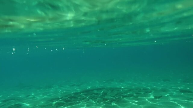 Beautiful beach in Ios island, Greece. View above and under the water. Sunrays shining through the clear blue water. Sandy bottom of the sea. Travel and summer vacation concept

