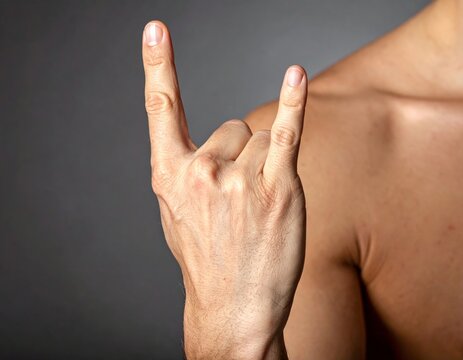 Male hand showing powerful rock and roll devil horns gesture against dark studio background, music, power, rebellion, energy, and success for concert, celebration, or communication concepts.
