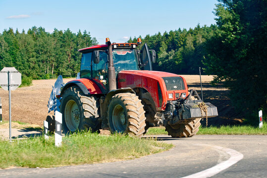 Minsk region, Belarus. Aug 7, 2022. Red tractor MTZ BELARUS. Oversized agricultural machine driving onto public roadway posing severe collision risk and traffic safety hazard for oncoming vehicles