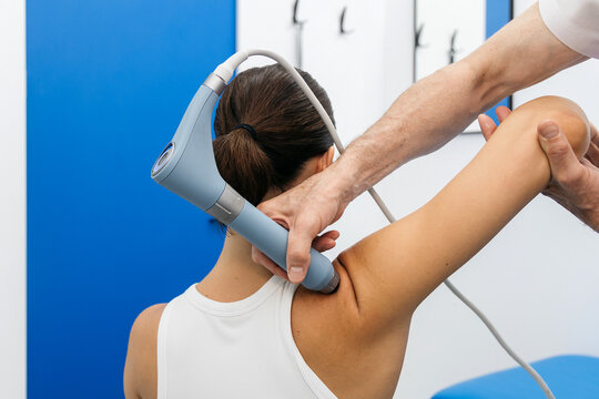 Young woman receiving non-invasive shockwave therapy in modern physiotherapy clinic. Concept rehabilitation, healthy movement and recovery process.
