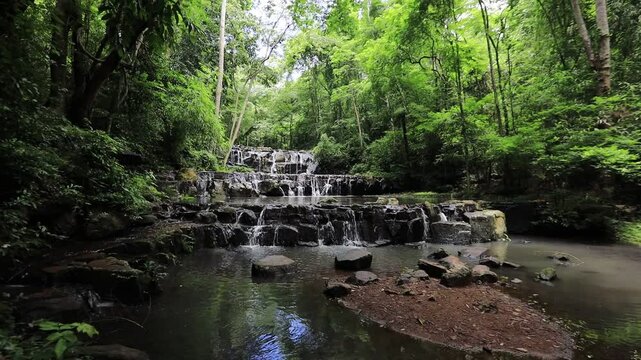 The video background features a natural landscape of a waterfall in a large forest. Sam Lan Waterfall in Saraburi National Park has beautiful flowing water.