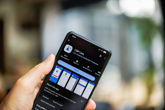Close-up of a hand holding a smartphone displaying the CBP Link app interface on Google Play Store