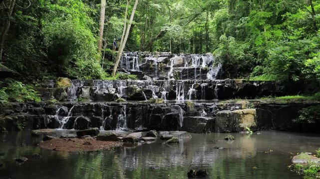 The video background features a natural landscape of a waterfall in a lush forest. Sam Lan Waterfall in Saraburi National Park boasts beautiful flowing water surrounded by diverse flora.