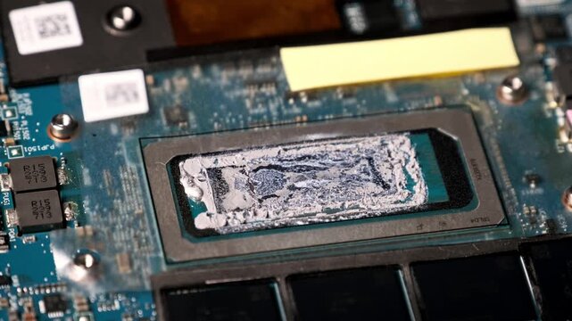 A macro close-up pans across a rectangular processor core with used thermal paste. The details of the surrounding printed circuit board and memory chips are clearly visible.