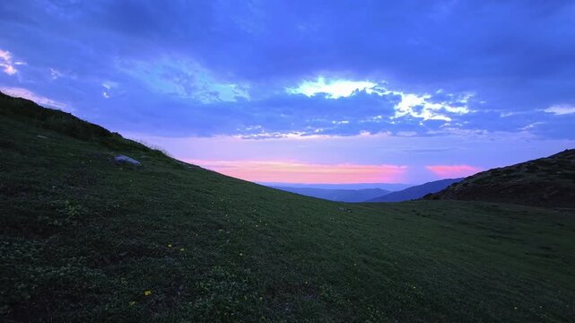 Open grassy mountain pass beneath blue clouds and pink sunset horizon