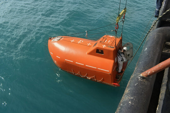 orange lifeboat lowered from ship into sea water during safety drill